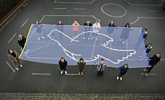 Bild: Die Klassensprecher der Regelschule sowie Schulsozialarbeiterin Anna Laura Schneegans (obere Reihe, Erste von rechts) und Werkenlehrer Jens Arand (obere Reihe, Zweiter von rechts) pr&auml;sentieren das Friedensbanner. 